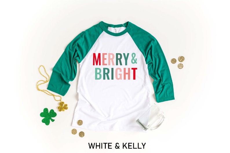 Puede incluir: Camiseta de b&eacute;isbol blanca y verde con el texto "Merry & Bright" en rojo, rosa y verde.