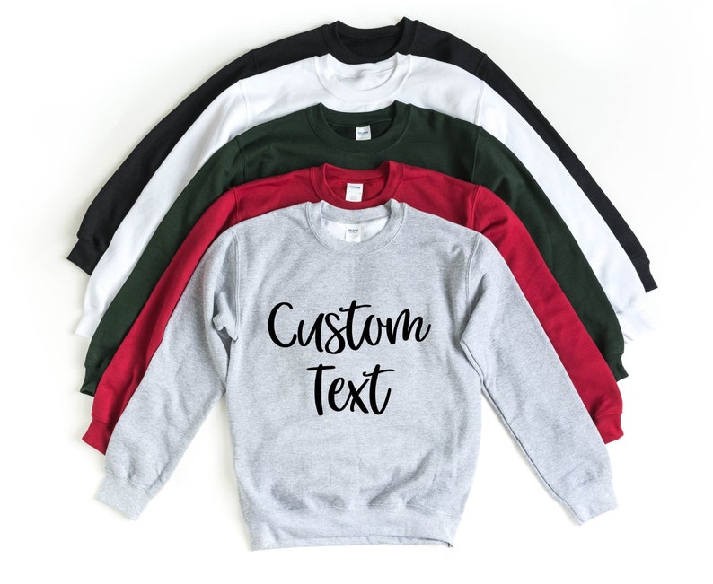 May include: A stack of sweatshirts in various colors, including black, white, green, red, and gray. The gray sweatshirt has the text "Custom Text" printed on the front in black.
