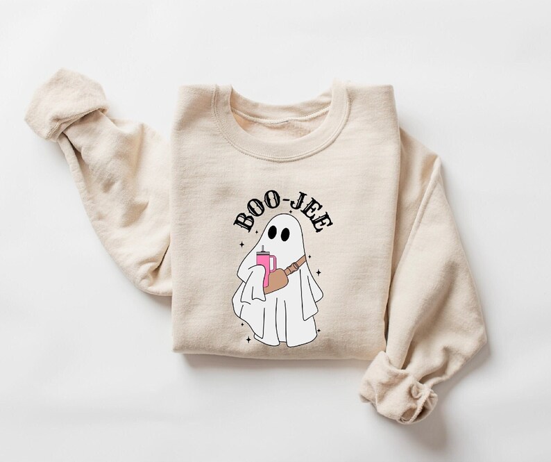May include: A beige sweatshirt with a ghost holding a pink drink and a black bag. The text "BOO-JEE" is above the ghost.