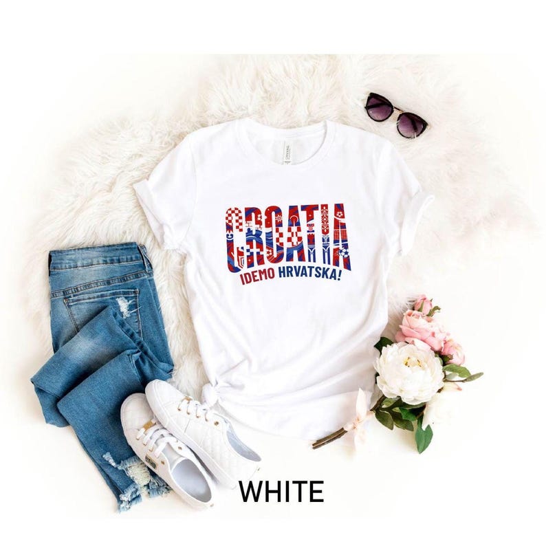 May include: A white t-shirt featuring the text CROATIA and IDEMO HRVATSKA in red, white, and blue patterns, paired with blue denim jeans, white sneakers, and black sunglasses. The shirt design incorporates a checkered motif and soccer ball graphics.