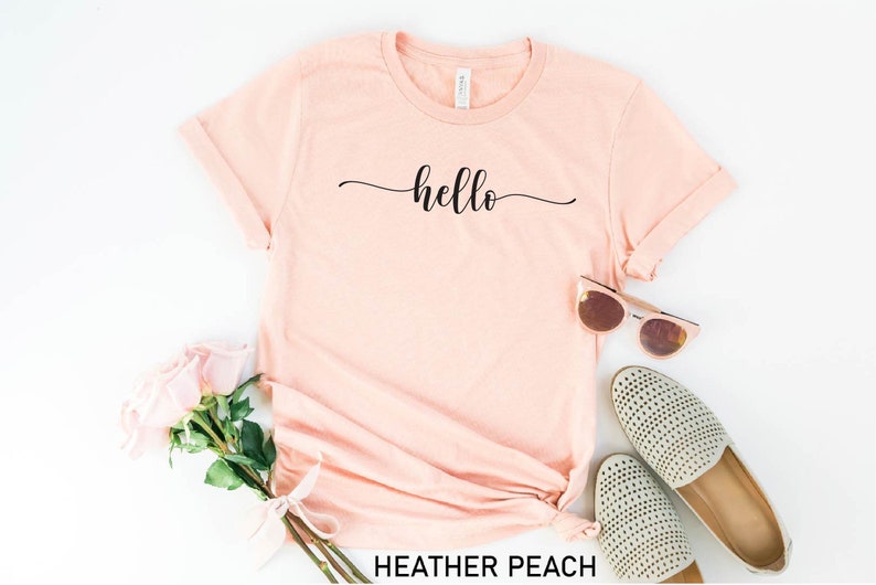 May include: A heather peach colored t-shirt with the word "hello" written in a cursive font on the front.
