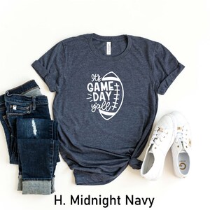 K&ouml;nnte beinhalten: Ein dunkelblaues T-Shirt mit einer wei&szlig;en Grafik eines Fu&szlig;balls und dem Text "It's Game Day y'all".
