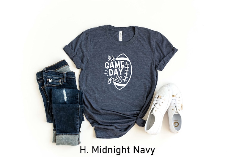 K&ouml;nnte beinhalten: Ein dunkelblaues T-Shirt mit einer wei&szlig;en Grafik eines Fu&szlig;balls und dem Text "It's Game Day y'all".