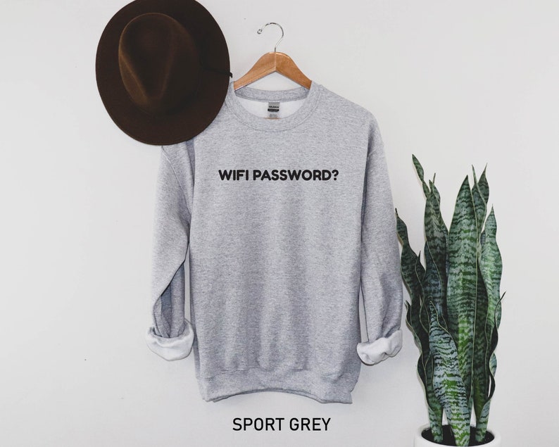 K&ouml;nnte beinhalten: Ein grauer Pullover mit dem Aufdruck "WIFI PASSWORD?" in Schwarz auf der Vorderseite. Der Pullover h&auml;ngt an einem Holzb&uuml;gel vor einer wei&szlig;en Wand. Der Text "SPORT GREY" ist unter dem Pullover aufgedruckt.