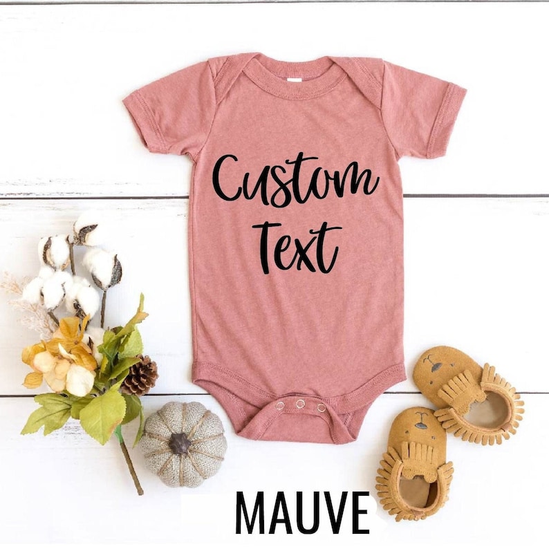 May include: Mauve baby onesie with short sleeves and snaps. The onesie has the text "Custom Text" printed on the front in black.