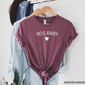 May include: Heather maroon t-shirt with the text "90's Baby" and a white heart.
