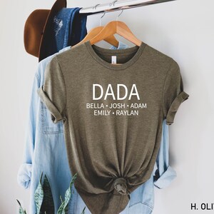 May include: Olive green t-shirt with the word "DADA" printed in white on the front. Below the word "DADA" are the names "BELLA, JOSH, ADAM, EMILY, RAYLAN" printed in white.