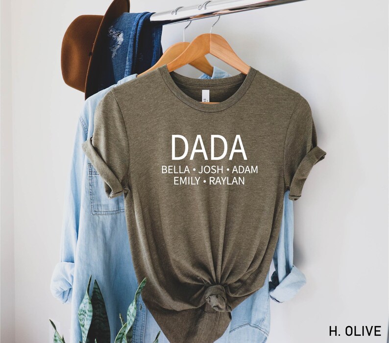 May include: Olive green t-shirt with the word "DADA" printed in white on the front. Below the word "DADA" are the names "BELLA, JOSH, ADAM, EMILY, RAYLAN" printed in white.
