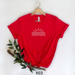May include: Red t-shirt with a white outline of a sun setting over waves.