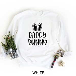 K&ouml;nnte beinhalten: Wei&szlig;er Pullover mit schwarzen Hasenohren und dem Aufdruck "Daddy Bunny" auf der Vorderseite.