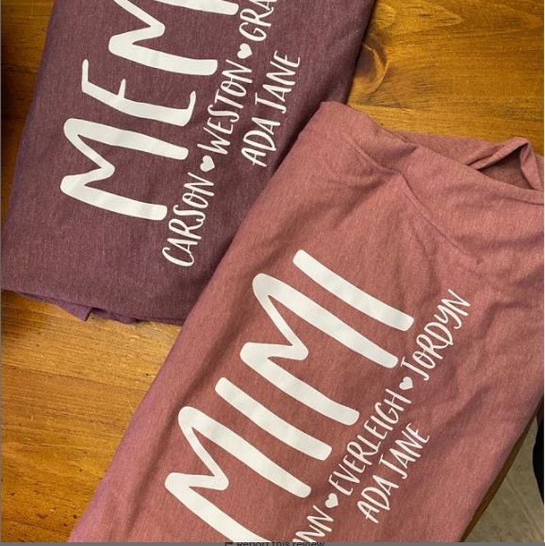 May include: Two maroon t-shirts with the word "Mimi" printed in white on the front. The shirts have the names of the grandchildren printed below the word "Mimi" with a heart symbol between each name. The names on the top shirt are "Carson", "Weston", "Grayson", and "Ada Jane". The names on the bottom shirt are "Everleigh", "Jordan", "Ada Jane".