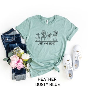 May include: A heather dusty blue t-shirt with a graphic of potted plants and the text "Just One More".