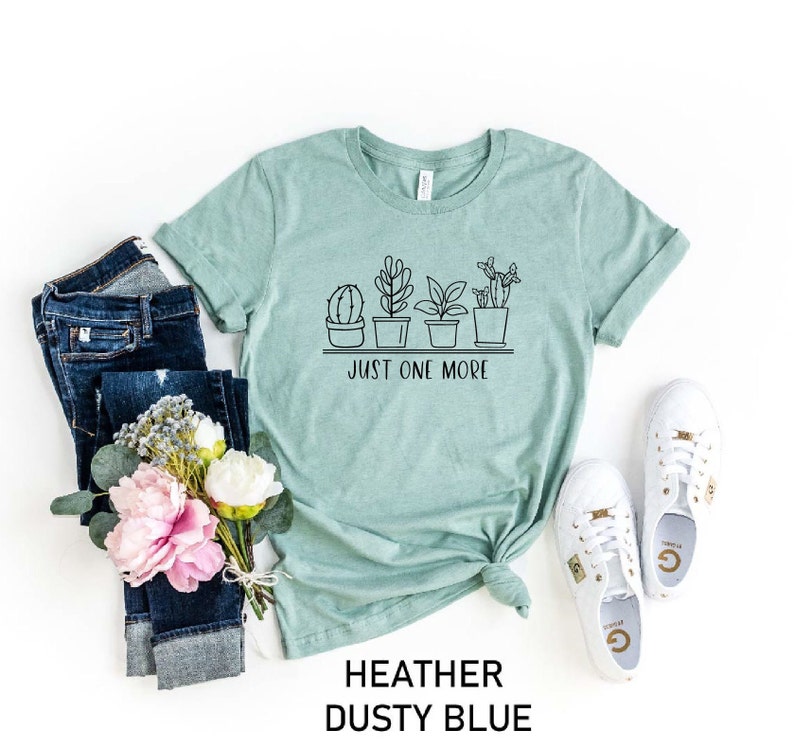 May include: A heather dusty blue t-shirt with a graphic of potted plants and the text "Just One More".
