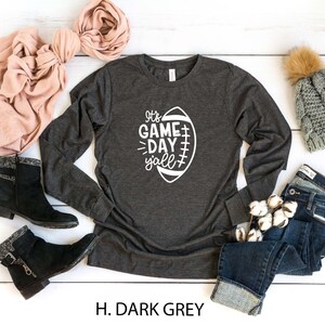 K&ouml;nnte beinhalten: Ein dunkelgraues Langarmshirt mit einer wei&szlig;en Grafik eines Fu&szlig;balls und dem Text "It's Game Day Y'all".