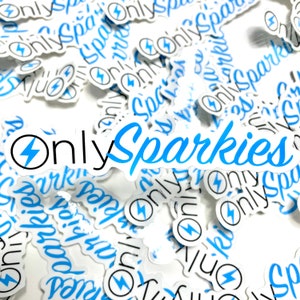 Puede incluir: Primer plano de una pila de pegatinas blancas con un diseño de rayo azul y negro. Las pegatinas dicen "Only Sparkies" en una fuente azul y negra.