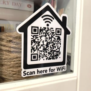Könnte beinhalten: Ein weißer Aufkleber mit einer schwarzen Hausform und einem schwarzen QR-Code darin. Der Aufkleber hat den Text "Scan here for WiFi" unten.