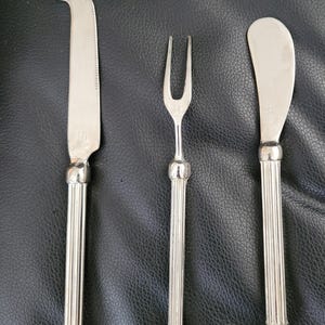 Peut inclure: Un ensemble de trois ustensiles argentés pour servir le fromage. L'ensemble comprend un couteau à fromage, une fourchette à fromage et un épandeur à fromage.