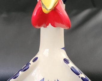 May include: A white ceramic rooster figurine with blue and gold accents. The rooster has a red comb and wattle, and its body is decorated with blue floral patterns.
