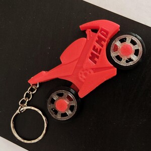 Puede incluir: Un llavero de moto rojo con una cadena plateada. La moto tiene una rueda negra y plateada y la palabra "MEMO" está impresa en el lateral.