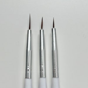May include: Three silver and white detail paint brushes with fine tips.