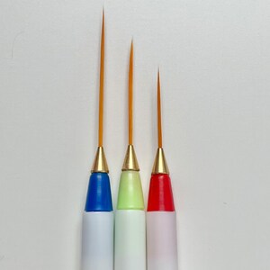 May include: Three paint brushes with different colored handles: blue, green, and red. The brushes have fine tips and are ideal for detail work.