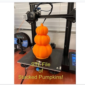 May include: A 3D printed stack of orange pumpkins on a black print bed of a 3D printer. The text "STL File of Stacked Pumpkins!" is below the print bed.
