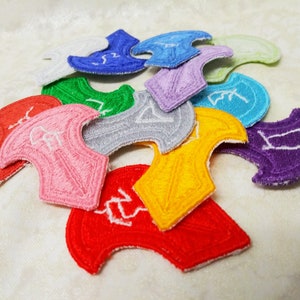 Könnte beinhalten: Eine Sammlung von zehn bunten gestickten Aufnähern in verschiedenen Formen, darunter eine Schildform, mit weißen Nähten. Die Aufnäher liegen auf einer weißen Oberfläche in einem Stapel.