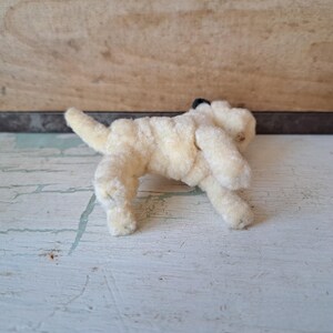 Pu&ograve; includere: Un piccolo giocattolo a forma di cane in peluche, in stile vintage, di colore crema chiaro. Il cane &egrave; in posa giocosa, con la coda sollevata. Il giocattolo ha un naso nero ed &egrave; realizzato in un materiale morbido e strutturato.