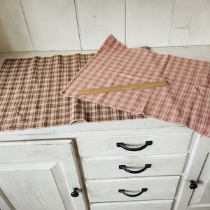 May include: Two rectangular woven fabric mats with a plaid pattern, one in brown and white and the other in red and white. A wooden ruler is placed across the red and white mat, showing a length measurement of approximately 12 inches.