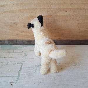 Pu&ograve; includere: Piccola statuetta di cane fatta a mano, con corpo color crema e orecchie e naso neri. Il cane ha una piccola macchia marrone sul fianco e una coda soffice. Il giocattolo &egrave; in piedi sulle zampe posteriori.
