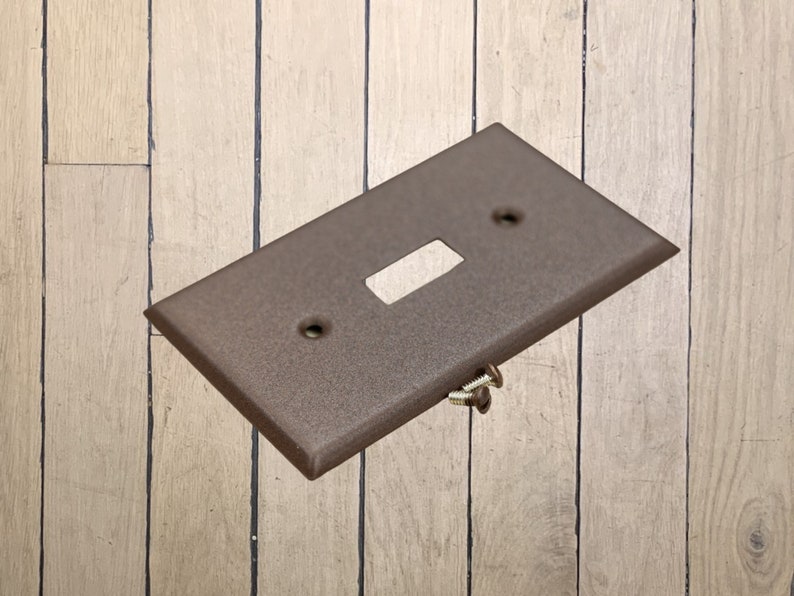 May include: A walnut brown metal single-gang electrical switch plate with two screw holes and a single switch cutout.