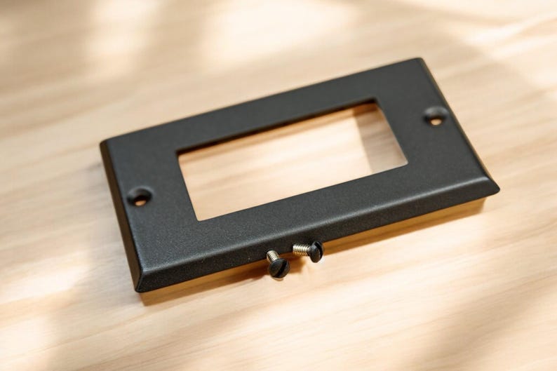 May include: A black metal plate with a rectangular cutout. Two black screws are visible on the bottom edge.