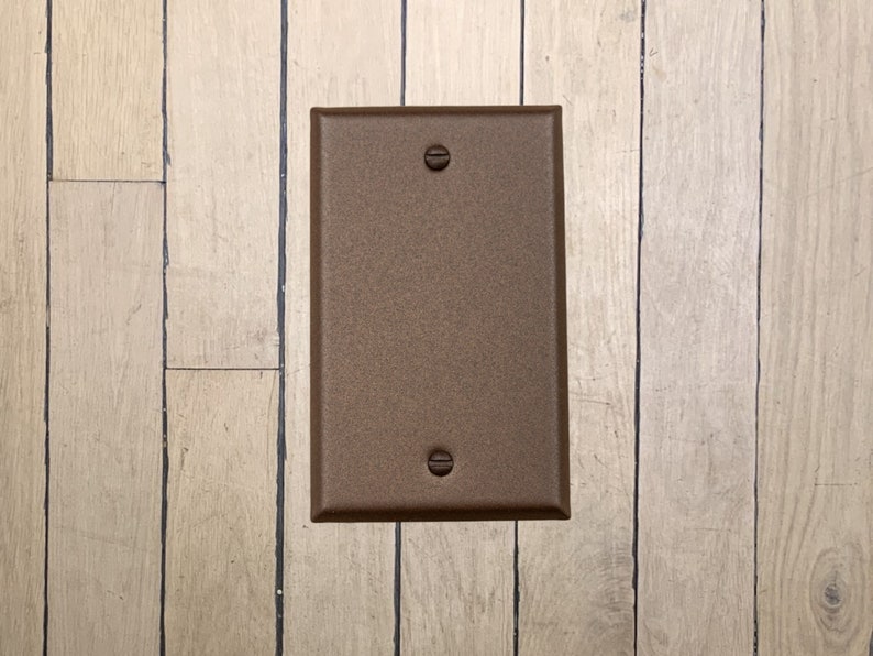 May include: A walnut brown metal electrical outlet cover plate with two screw holes.
