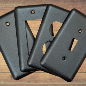 May include: Four black plastic wall plates with different outlet configurations. The plates have a textured finish and are designed to cover electrical outlets.
