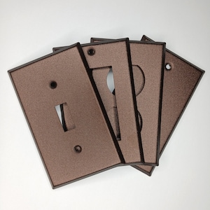 May include: A set of four brown metal light switch and outlet covers. The covers have a textured finish and are designed to match a rustic or industrial decor.