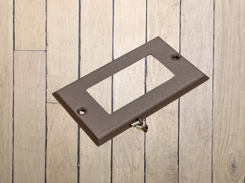 May include: A walnut brown metal electrical outlet cover plate with two screw holes and two screws.