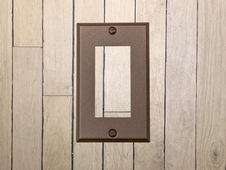 May include: A walnut brown metal wall plate with a rectangular opening for an electrical outlet. The plate has two small screws on the top and bottom.