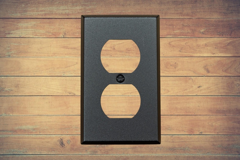 A single black metal duplex plate with two openings and a matching screw installed. It has a brown wood background.