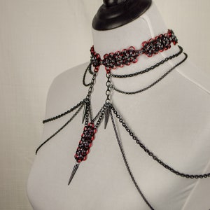 May include: A black and red chainmail choker necklace with multiple black chains and spikes hanging from it.