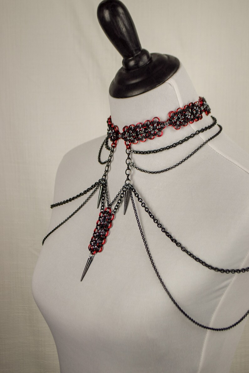 May include: A black and red chainmail choker necklace with multiple black chains and spikes hanging from it.
