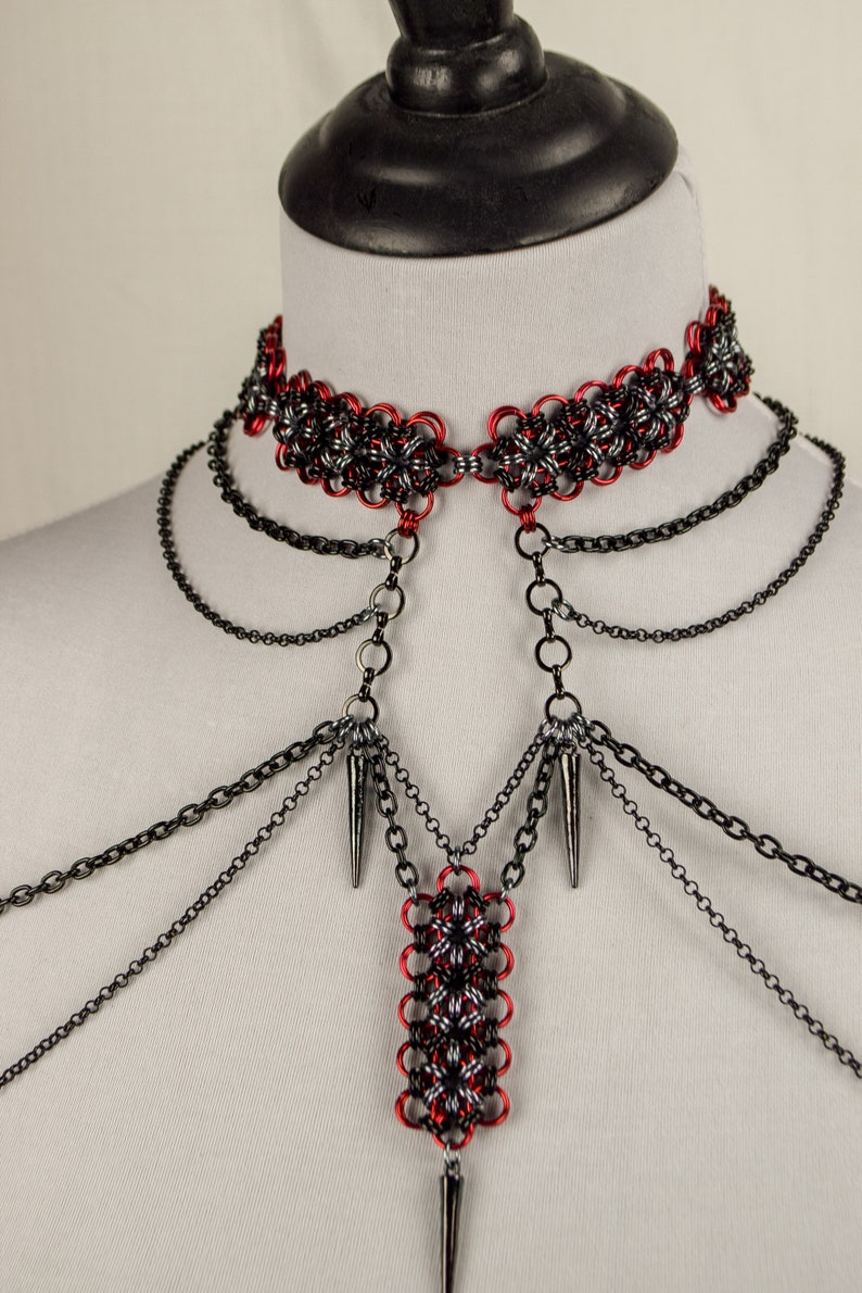 May include: A red and black chainmail choker necklace with multiple black chain strands and spikes hanging from the bottom.
