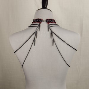 May include: A black chain choker necklace with red and black beads and silver spikes. The necklace is on a white mannequin.