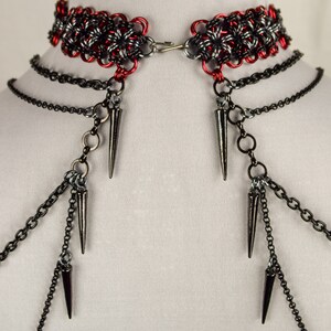 May include: A red and black chainmail choker with multiple black chains and spikes hanging from it.