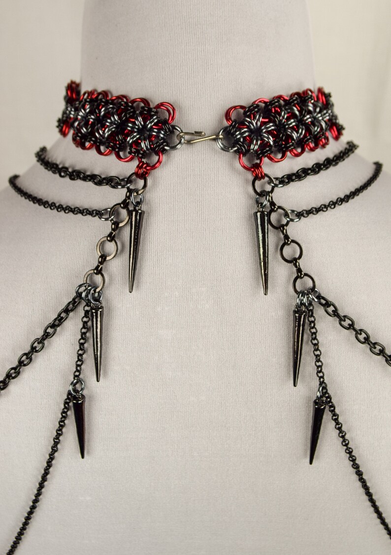 May include: A red and black chainmail choker with multiple black chains and spikes hanging from it.