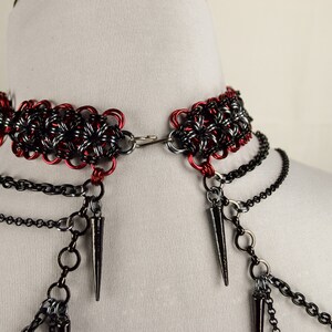 May include: A black and red chainmail choker necklace with multiple black chain strands and spikes hanging from the bottom.