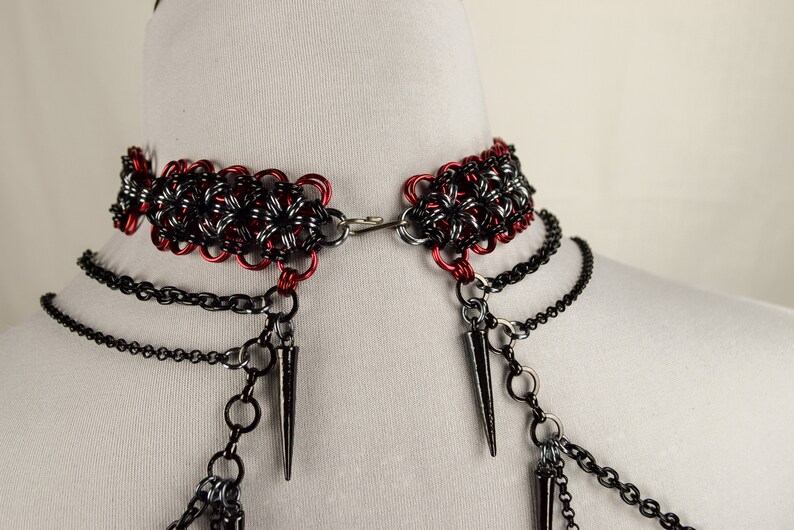 May include: A black and red chainmail choker necklace with multiple black chain strands and spikes hanging from the bottom.