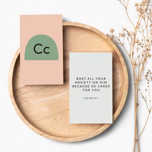 Könnte beinhalten: Zwei Karten mit hellgrünem und rosafarbenem Hintergrund. Die erste Karte hat einen grünen Halbkreis mit den Buchstaben "Cc" in Schwarz. Die zweite Karte hat den Text "CAST ALL YOUR ANXIETY ON HIM BECAUSE HE CARES FOR YOU. 1 PETER 5:7" in Schwarz.