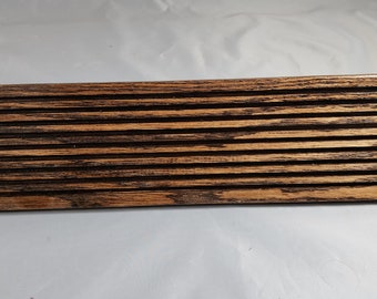 Puede incluir: Una decoración de pared de madera marrón oscuro con un diseño de listones. La madera tiene un patrón de veta natural y está teñida de un color marrón oscuro.