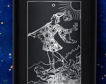 May include: Black metal flask with a silver engraving of the Fool tarot card. The Fool is depicted as a young man walking towards a cliff with a staff and a dog. The card reads "THE FOOL."