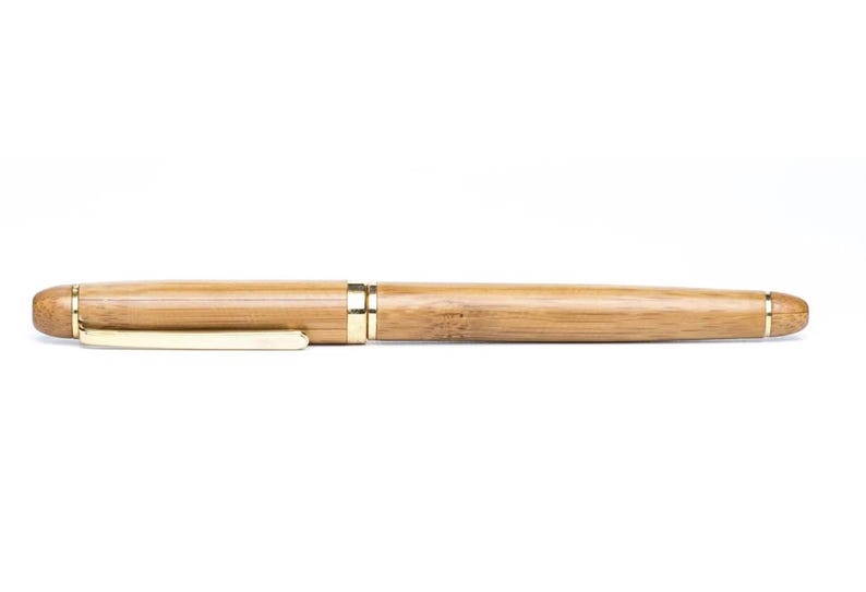 Puede incluir: Un bol&iacute;grafo de bamb&uacute; con acabado natural y detalles dorados. El bol&iacute;grafo tiene un clip dorado y una banda dorada cerca de la punta. Es un instrumento de escritura.